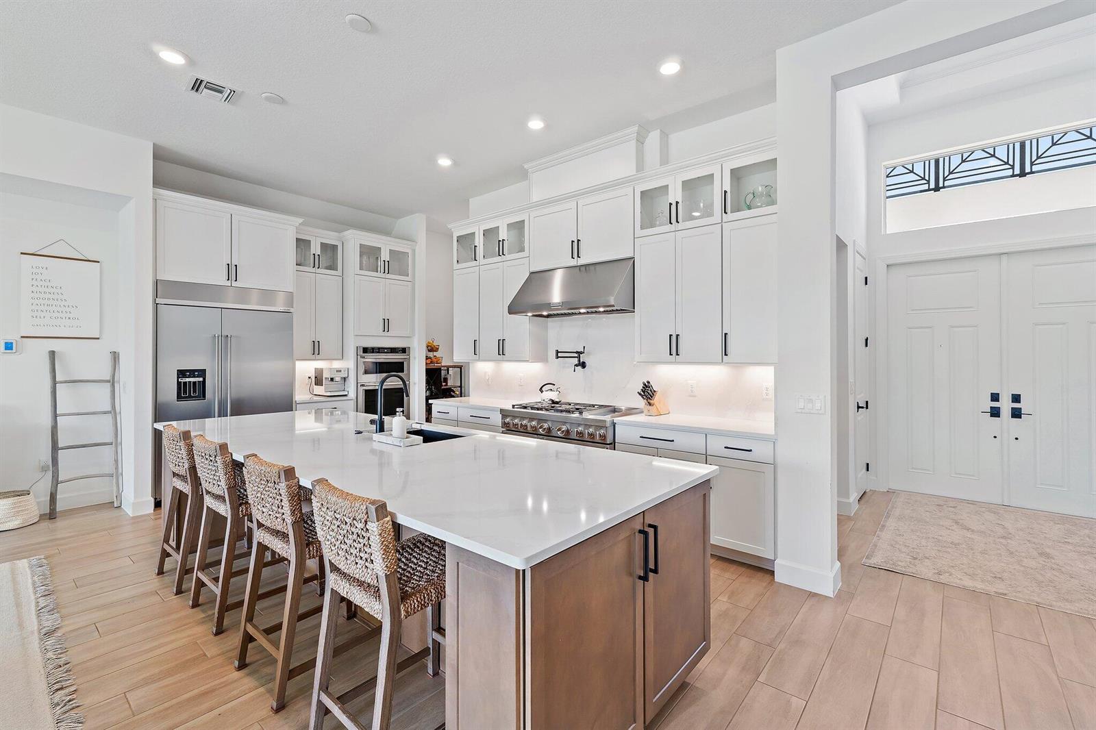 A modern kitchen features white cabinetry, a large quartz island, and wood-look tile flooring — 20161 SE Bridgewater Drive, Jupiter FL 33458, JUPITER, FL