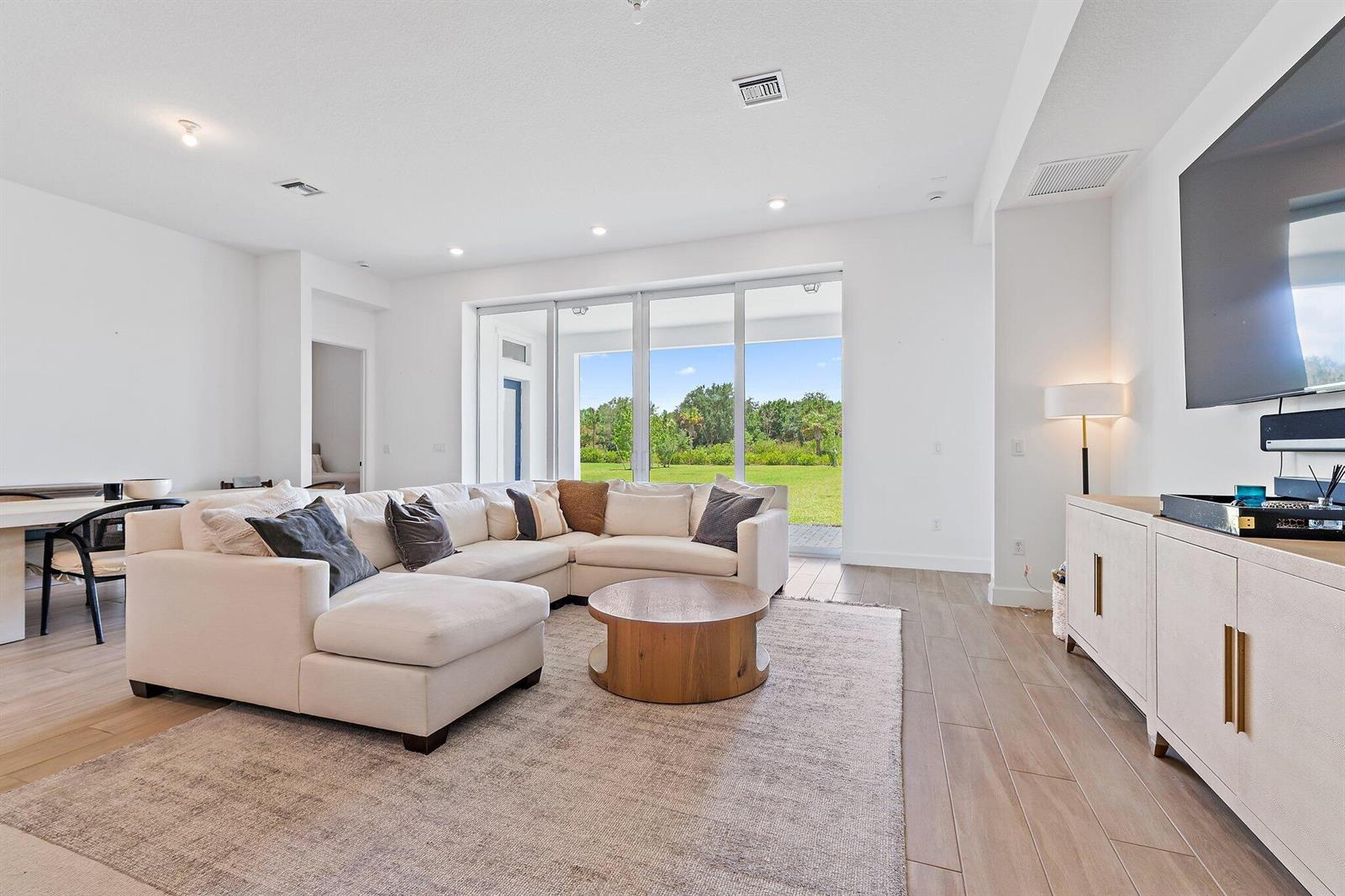 A bright living room features a white sectional sofa, wood coffee table, and sliding glass doors — 20161 SE Bridgewater Drive, Jupiter FL 33458, JUPITER, FL