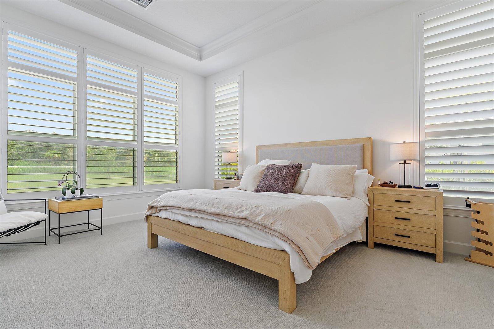 A bright bedroom features a light wood bed frame, neutral bedding, and white plantation shutters — 20161 SE Bridgewater Drive, Jupiter FL 33458, JUPITER, FL