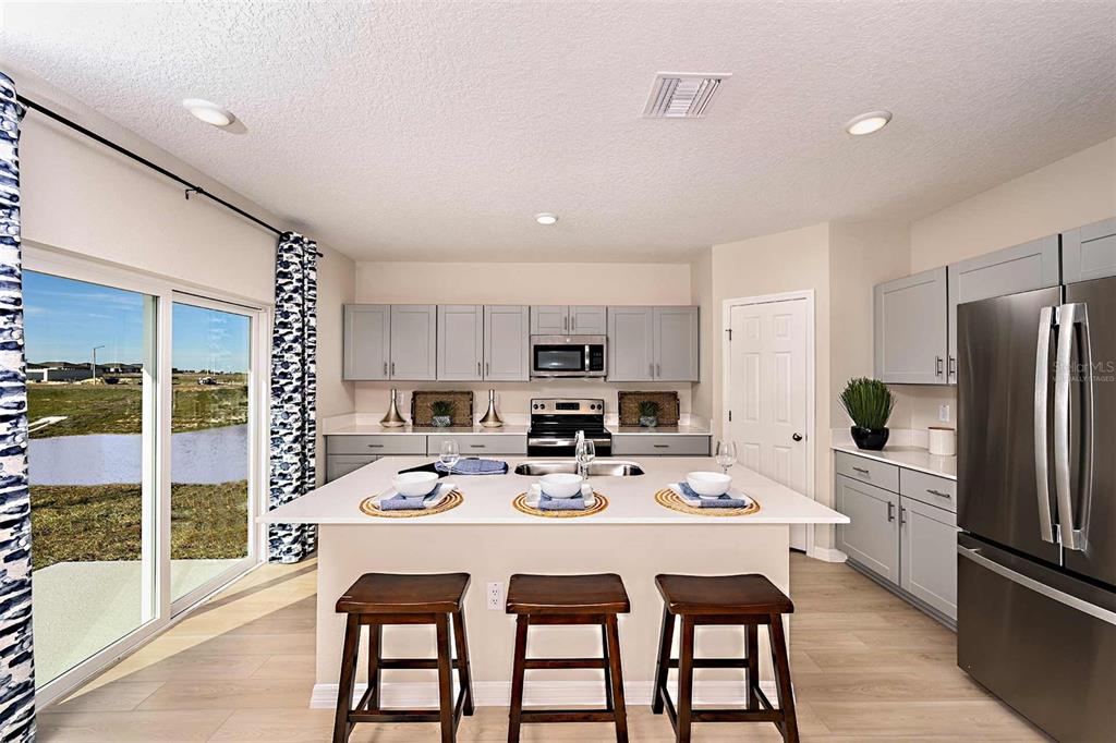 A kitchen features light gray cabinets, a white island with three stools, and sliding glass doors — 5019 OAKS RIVER STREET, DAVENPORT, FL