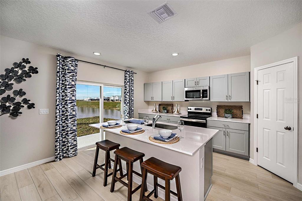 A kitchen with a center island, grey cabinets, and a sliding door overlooking a pond — 5019 OAKS RIVER STREET, DAVENPORT, FL