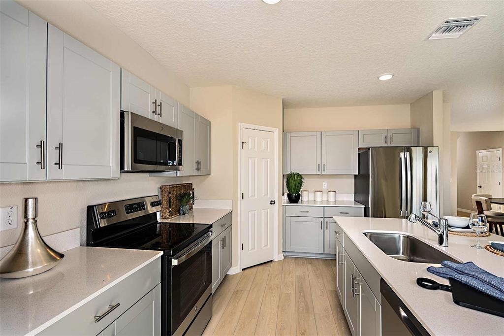 A modern kitchen features light gray cabinets, stainless steel appliances, and a central island — 5019 OAKS RIVER STREET, DAVENPORT, FL