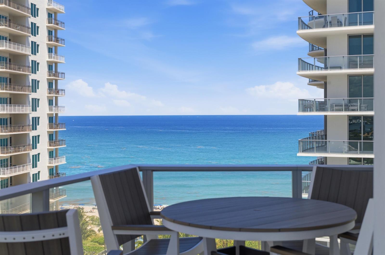 A balcony with a table and chairs overlooks the ocean between two high-rise buildings — 3100 N Ocean Drive # 1202, Singer Island FL 33404, SINGER ISLAND, FL