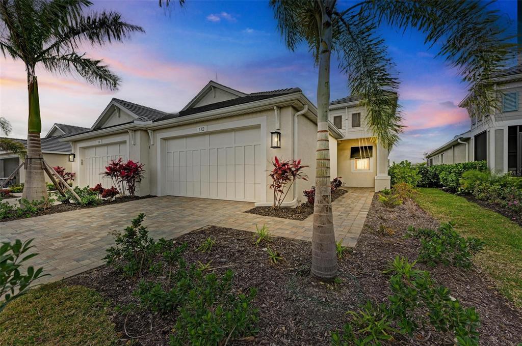 A beige single-story house with a two-car garage, paver driveway, and palm trees at dusk — 172 VAN GOGH COVE, BRADENTON, FL