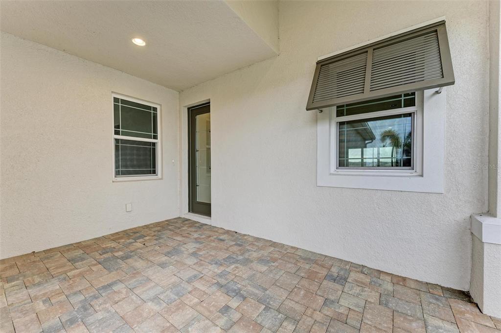 A covered patio features paver flooring, a glass door, and a window with a shutter — 172 VAN GOGH COVE, BRADENTON, FL