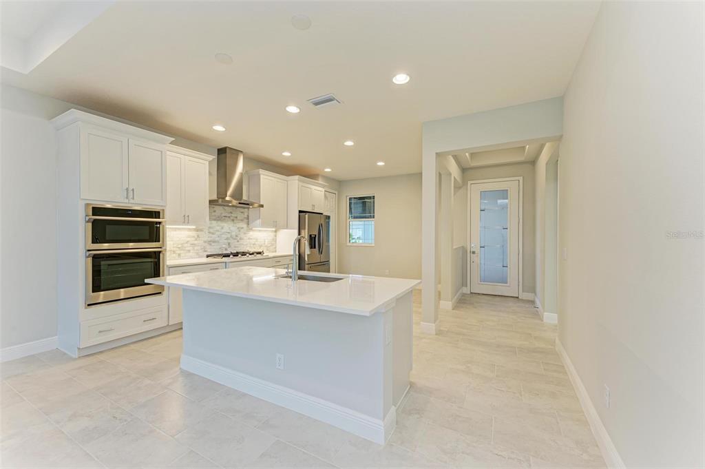 A modern kitchen features white cabinetry, a central island with a sink, and stainless appliances — 172 VAN GOGH COVE, BRADENTON, FL