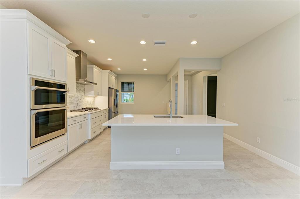 A modern kitchen features white cabinetry, a large central island, and stainless steel appliances — 172 VAN GOGH COVE, BRADENTON, FL