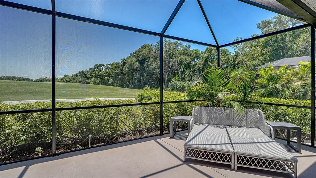 A screened-in patio features a light-colored daybed and views of a grassy field and trees — 7823 HERITAGE CLASSIC COURT, LAKEWOOD RANCH, FL