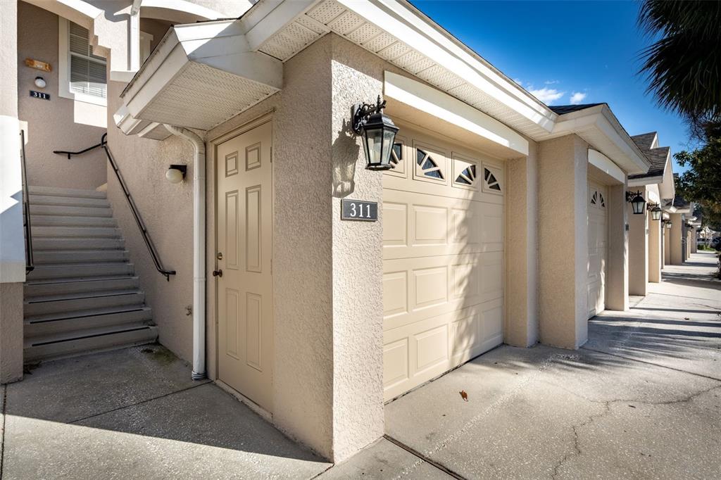 An exterior view shows a tan garage door, a side entry door, and concrete stairs — 9435 MYRTLE CREEK LANE UNIT 311, ORLANDO, FL