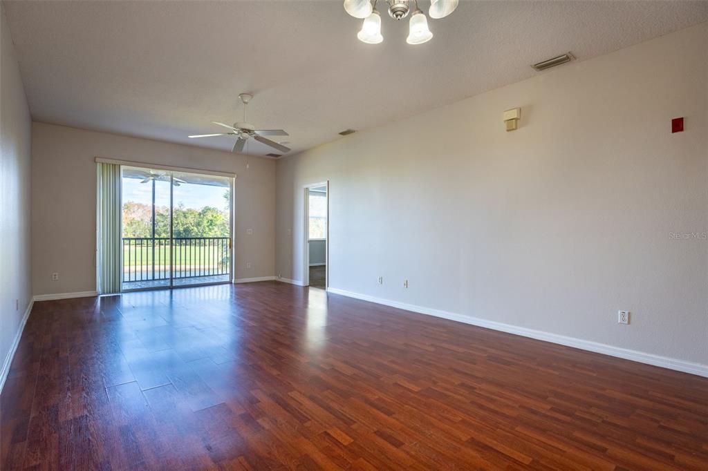 An empty living room features dark wood flooring, a ceiling fan, and a sliding glass door — 9435 MYRTLE CREEK LANE UNIT 311, ORLANDO, FL