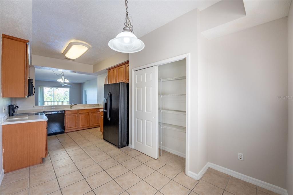 A kitchen with wood cabinets, black appliances, tile flooring, and an open pantry closet — 9435 MYRTLE CREEK LANE UNIT 311, ORLANDO, FL