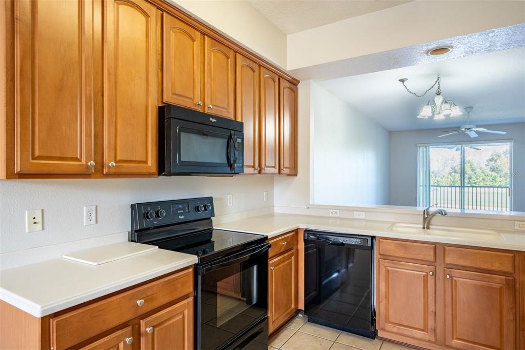 A kitchen features wood cabinets, black appliances, white countertops, and a view into the dining area — 9435 MYRTLE CREEK LANE UNIT 311, ORLANDO, FL