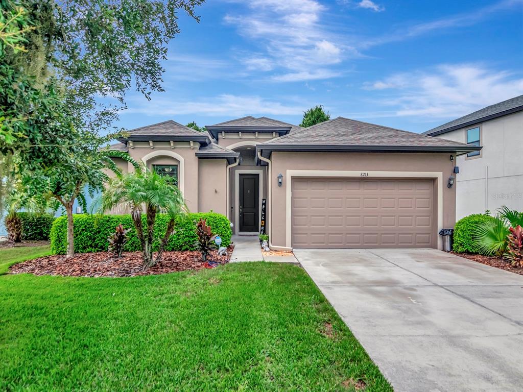 A single-story house with a tan stucco exterior, a two-car garage, and a landscaped front yard — 8213 SUMMER BROOK COURT, LAND O LAKES, FL