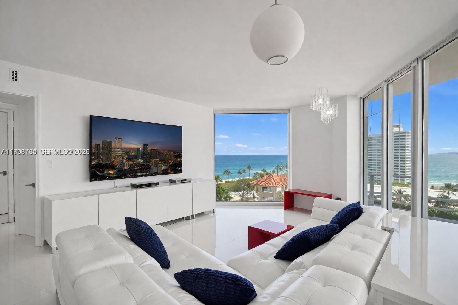 A modern living room features a white sectional sofa, a large television, and ocean views — 7330 Ocean Ter # C, Miami Beach FL 33141, MIAMI BEACH, FL