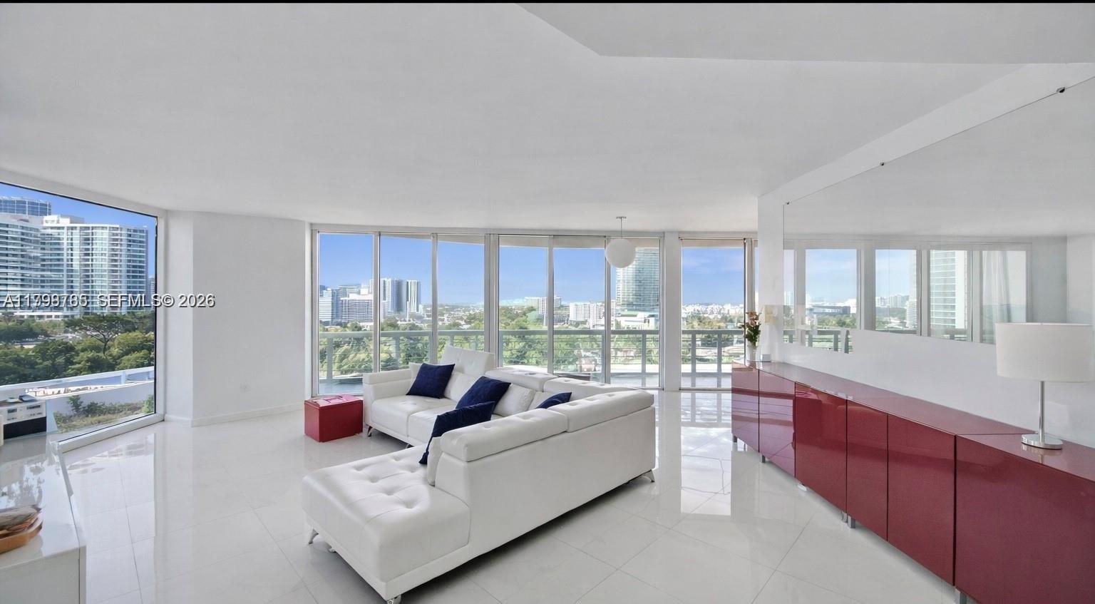 A bright living room features white tile floors, a white sectional sofa, and floor-to-ceiling windows — 7330 Ocean Ter # C, Miami Beach FL 33141, MIAMI BEACH, FL