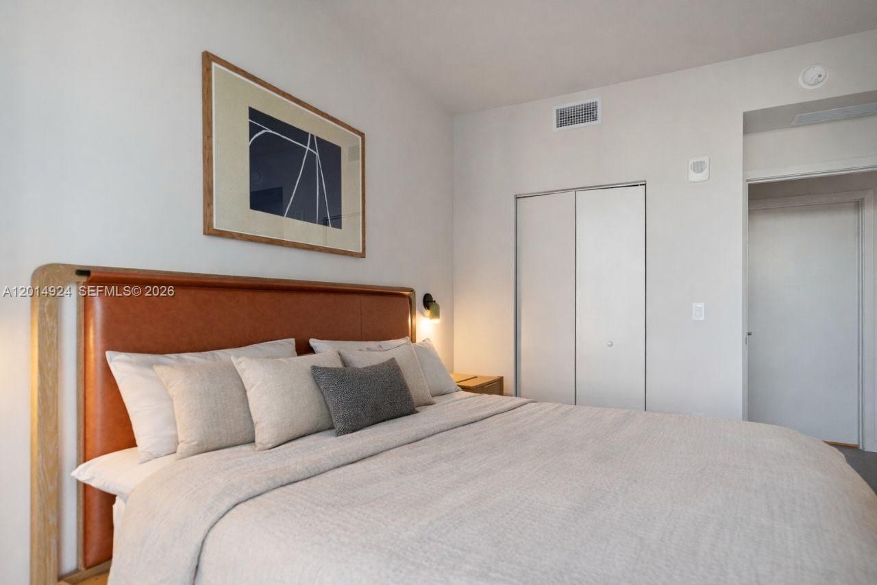 A bedroom features a leather headboard, neutral bedding, and a white closet — 11 NE 6th # 1210, Miami FL 33132, MIAMI, FL