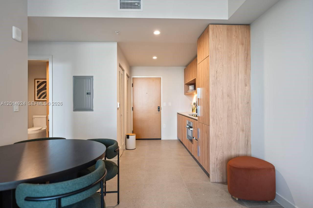This interior view shows a kitchen with wood cabinetry, a dining area, and a bathroom — 11 NE 6th # 1210, Miami FL 33132, MIAMI, FL