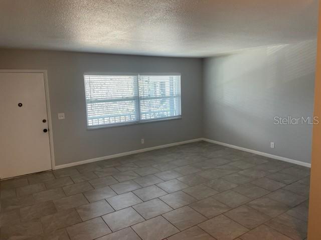 An empty room features gray walls, large gray floor tiles, and a white entry door — 675 INDIAN ROCKS ROAD N UNIT 106D, BELLEAIR BLUFFS, FL