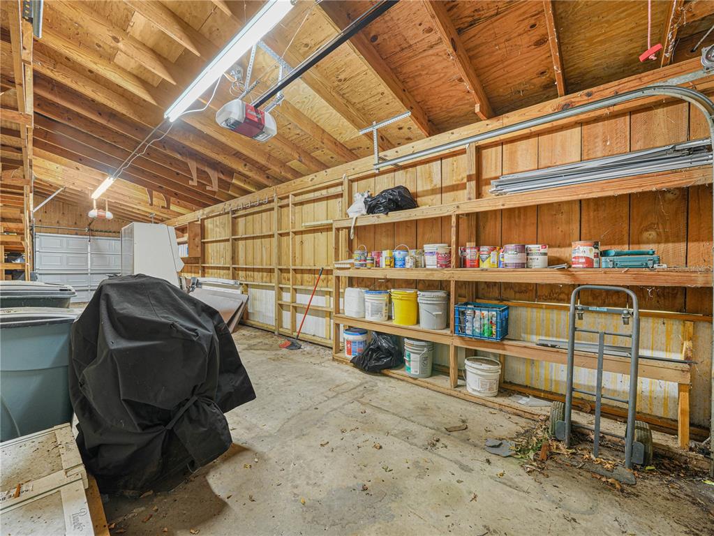 A garage interior features exposed wooden rafters, concrete flooring, and built-in wooden shelving units — 112 N POPLAR AVENUE, SANFORD, FL