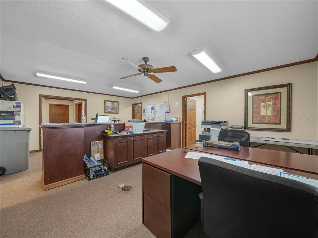 An office space features a wooden reception desk, a desk with a chair, and fluorescent lighting — 112 N POPLAR AVENUE, SANFORD, FL