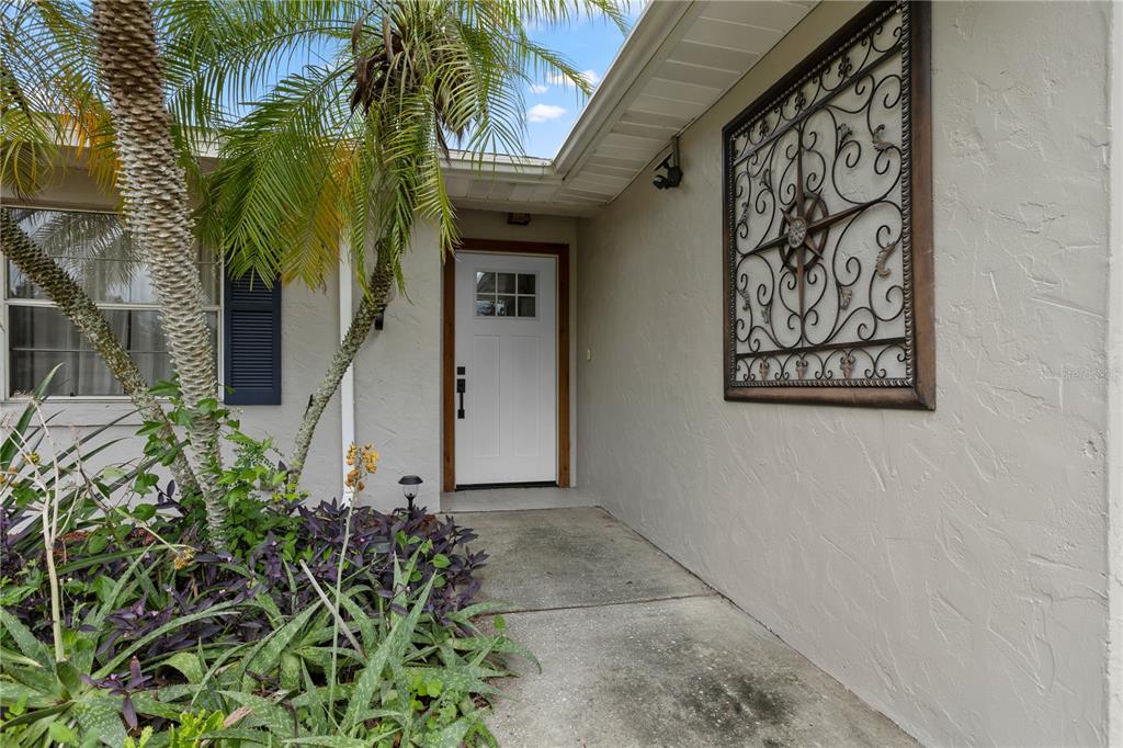 A white front door with a window sits under a covered entryway beside a palm tree — 630 E THELMA STREET, LAKE ALFRED, FL