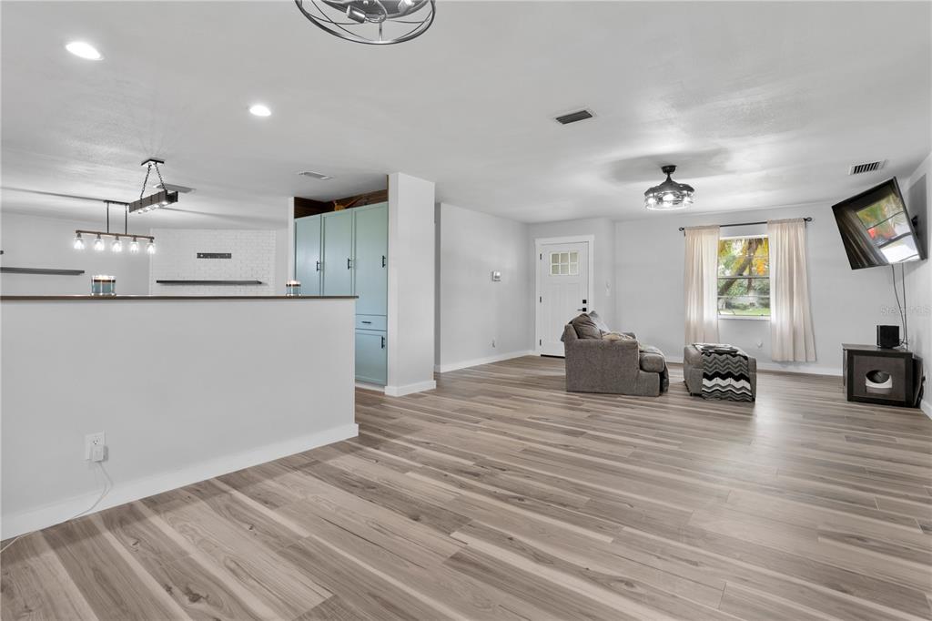 An open-concept living area features light wood-look flooring, a kitchen peninsula, and a mounted television — 630 E THELMA STREET, LAKE ALFRED, FL