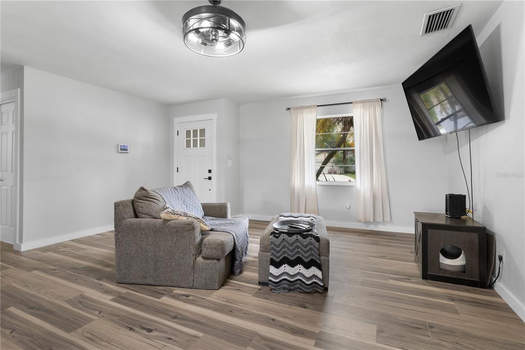 A living room features light gray walls, wood-look flooring, a gray armchair, and a wall-mounted television — 630 E THELMA STREET, LAKE ALFRED, FL