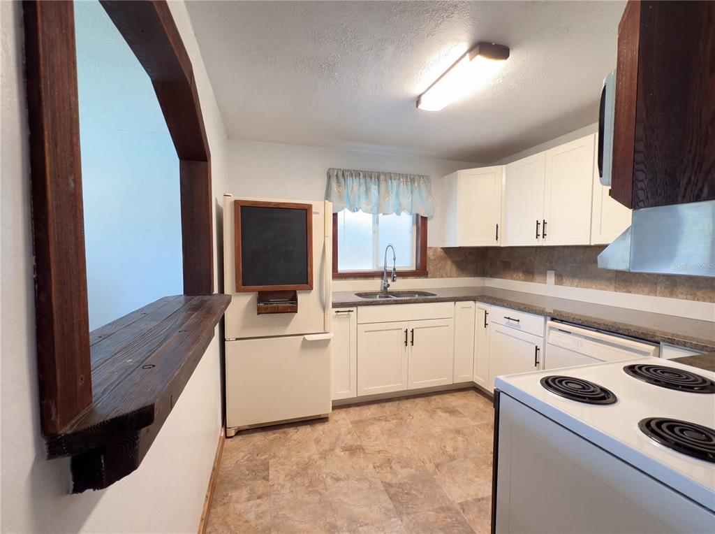 A kitchen features white cabinets, a refrigerator with a chalkboard, and a wooden pass-through counter — 1385 BENDER AVENUE, DAYTONA BEACH, FL