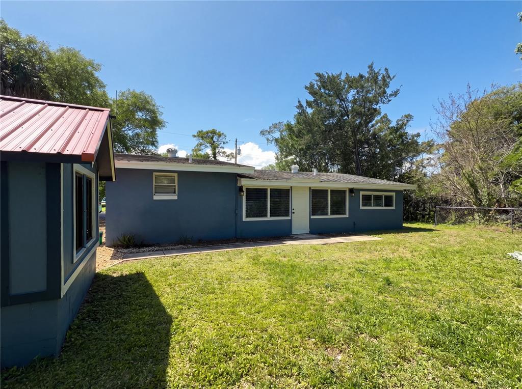 A blue house exterior with a red metal roof section and a grassy backyard — 1385 BENDER AVENUE, DAYTONA BEACH, FL