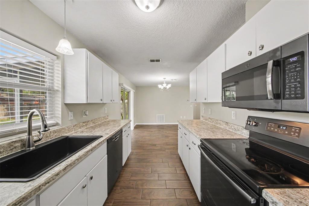 A galley-style kitchen features white cabinets, granite-look countertops, and dark appliances — 450 PARK GLEN DRIVE, TAVARES, FL