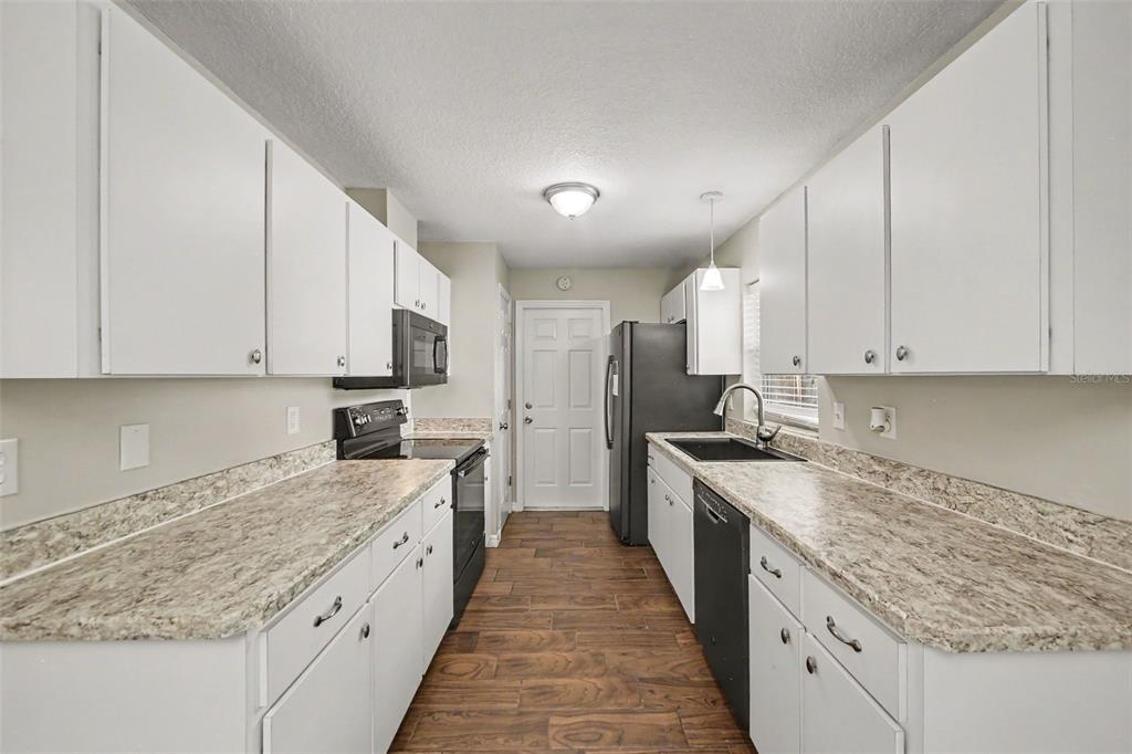 A galley kitchen features white cabinets, stone-look countertops, black appliances, and wood-look flooring — 450 PARK GLEN DRIVE, TAVARES, FL