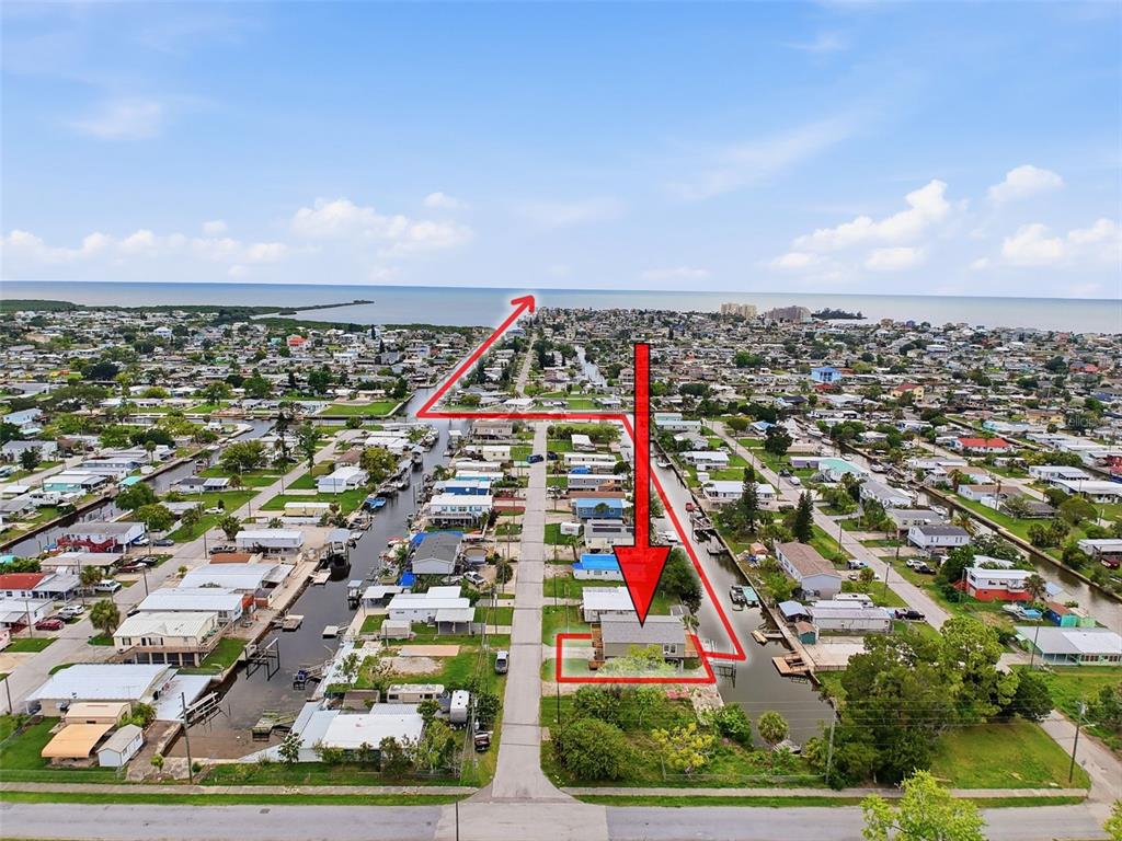 An aerial view shows a residential neighborhood with a canal-front house highlighted by red arrows — 6839 CURLEW LANE, HUDSON, FL