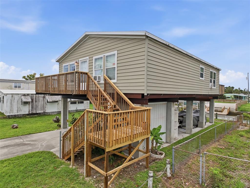 An elevated house with light green siding and a wooden staircase leading to a deck — 6839 CURLEW LANE, HUDSON, FL