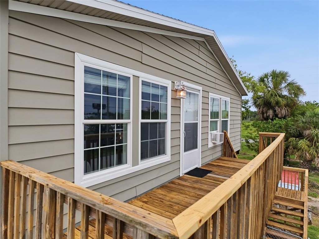 An exterior view of a house with light-colored siding, a wooden deck, and a staircase — 6839 CURLEW LANE, HUDSON, FL