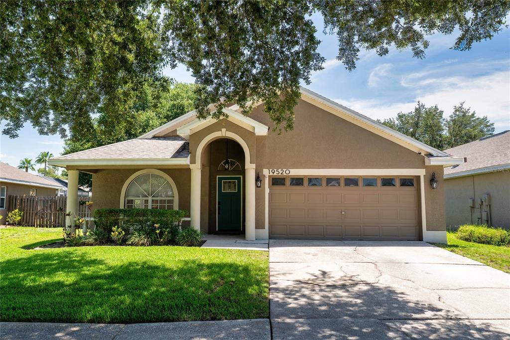 A single-story house with a tan stucco exterior, a two-car garage, and a covered entryway — 19520 MORDEN BLUSH DRIVE, LUTZ, FL