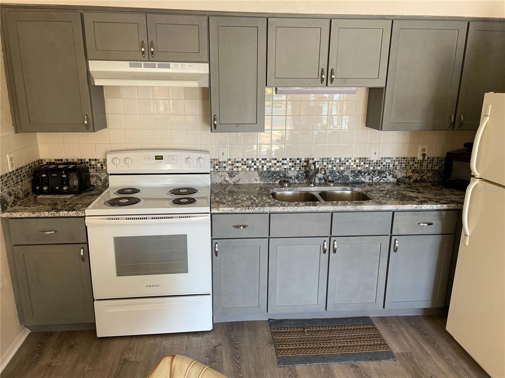 A kitchen features gray cabinets, granite countertops, a white stove, and a tiled backsplash — 4358 TAHITIAN GARDENS CIRCLE UNIT G, HOLIDAY, FL