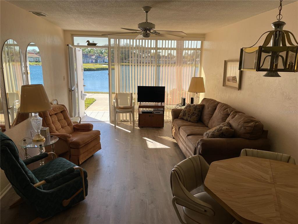 A living room with wood-look flooring, a brown sofa, armchairs, and a view of water — 4358 TAHITIAN GARDENS CIRCLE UNIT G, HOLIDAY, FL