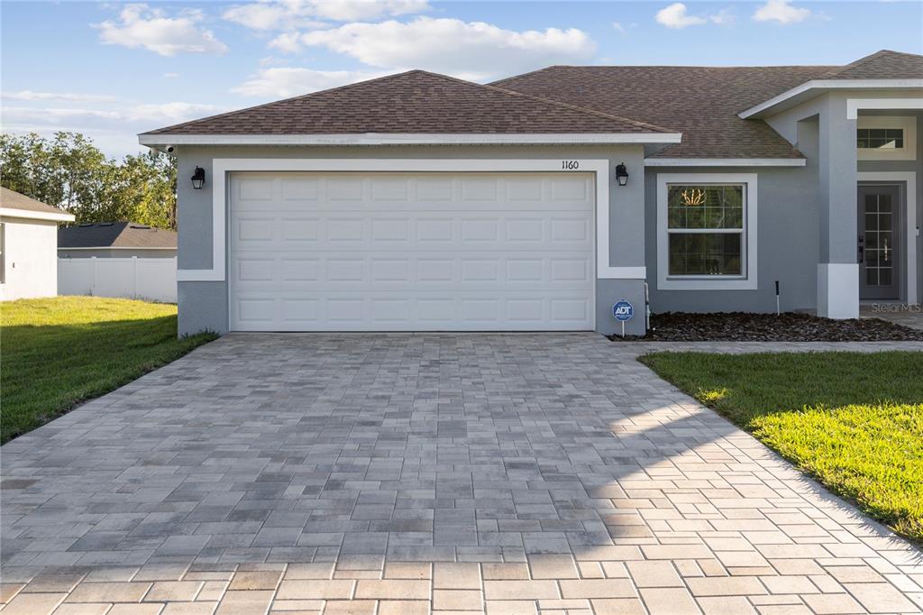 A gray house exterior features a two-car garage, a paved driveway, and a front entrance — 1160 NELSON MEADOW LANE, KISSIMMEE, FL