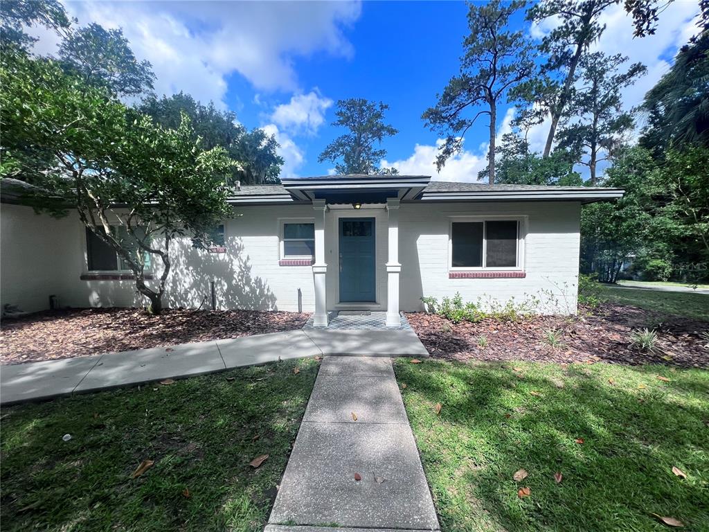 A single-story white brick house features a blue front door and a concrete walkway — 2707 NW 4TH AVENUE, GAINESVILLE, FL