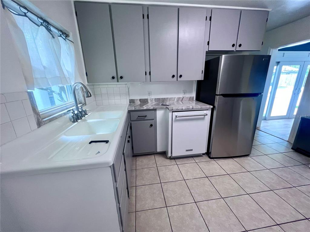 A kitchen features gray cabinets, a white double sink, a dishwasher, and a stainless refrigerator — 2707 NW 4TH AVENUE, GAINESVILLE, FL