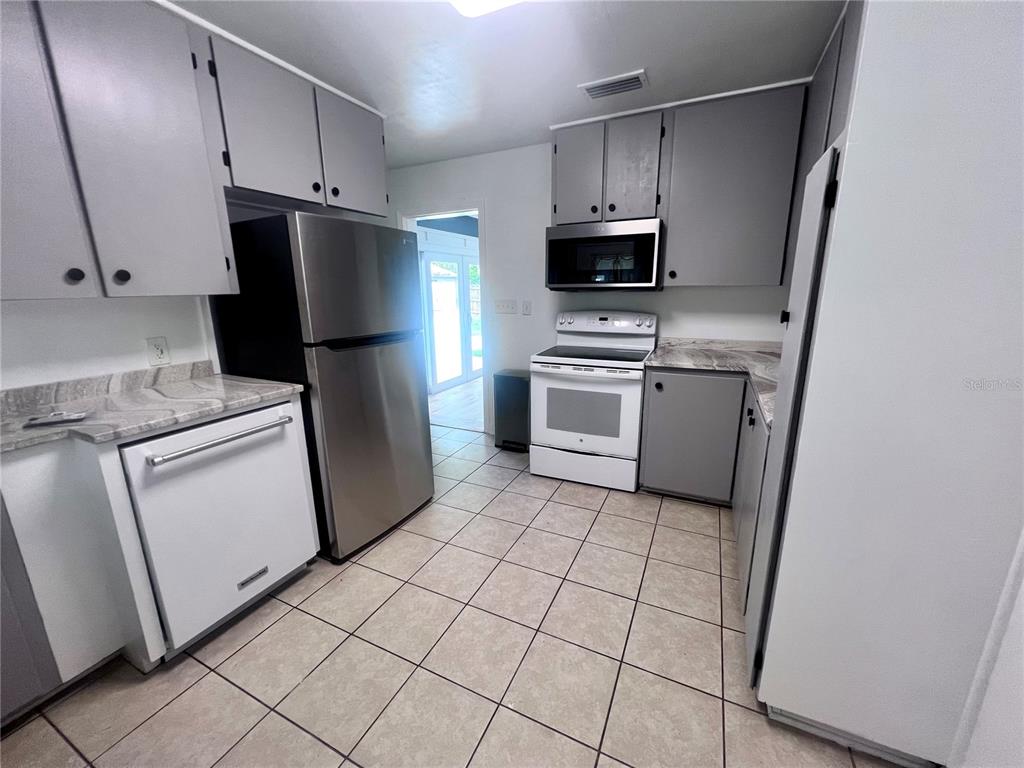 A kitchen features gray cabinets, stainless steel appliances, a white dishwasher, and tiled flooring — 2707 NW 4TH AVENUE, GAINESVILLE, FL