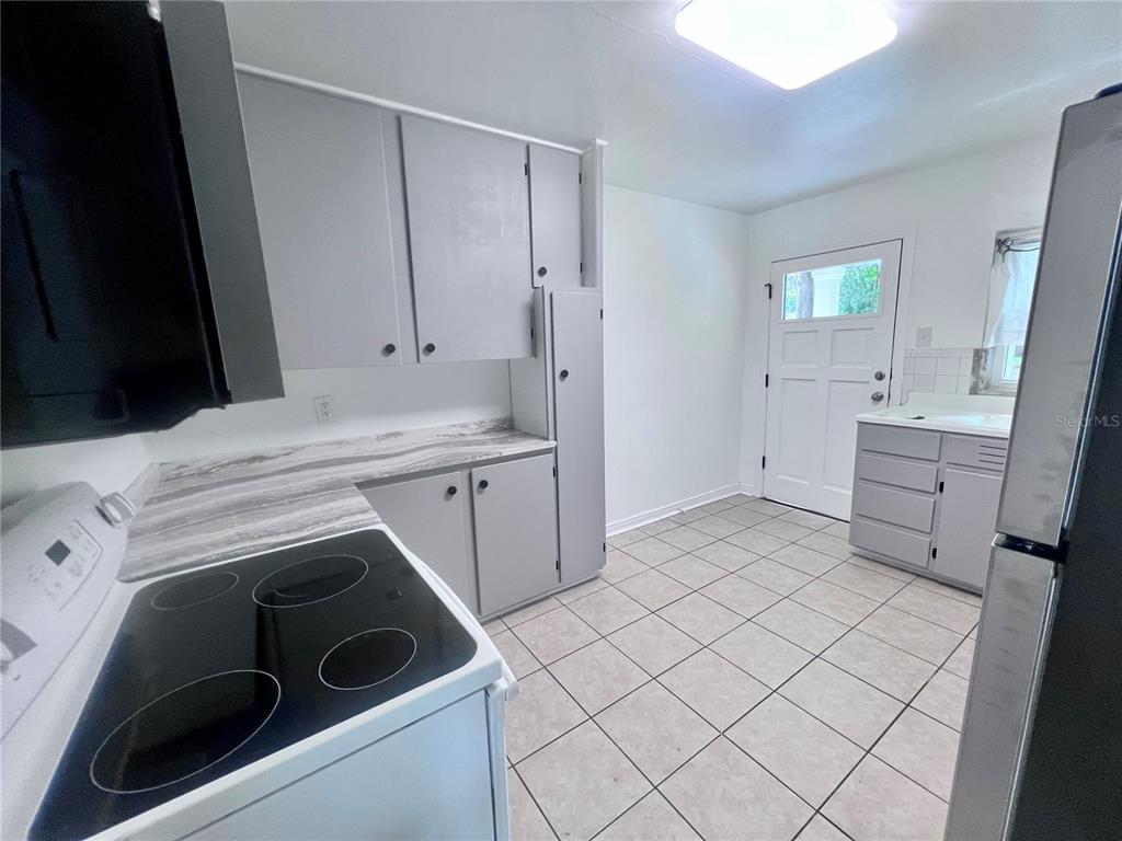 A kitchen features gray cabinets, marble-patterned countertops, a black electric stove, and tiled flooring — 2707 NW 4TH AVENUE, GAINESVILLE, FL