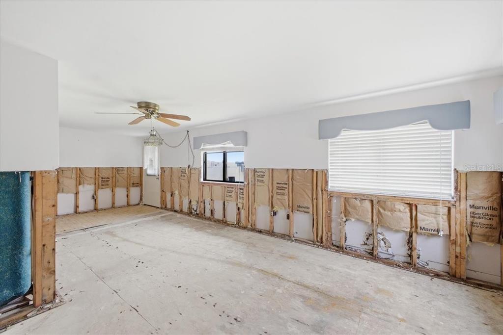 An unfinished room with exposed wall studs, fiberglass insulation, and a bare subfloor — 4436 106TH STREET W, BRADENTON, FL