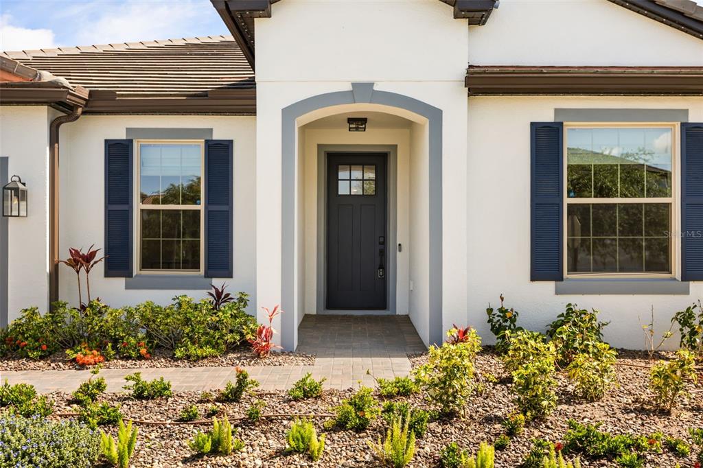A front exterior view of a house with a dark door, blue shutters, and landscaping — 7916 WANDERING WAY, ORLANDO, FL