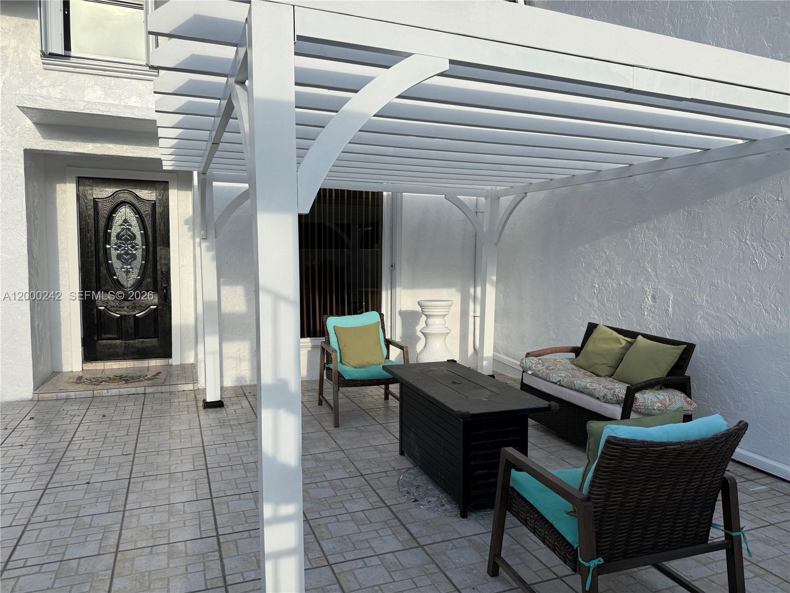 A patio features a white pergola, wicker furniture, and a fire pit on tiled flooring — 13505 NE 23rd Ct, North Miami FL 33181, NORTH MIAMI, FL