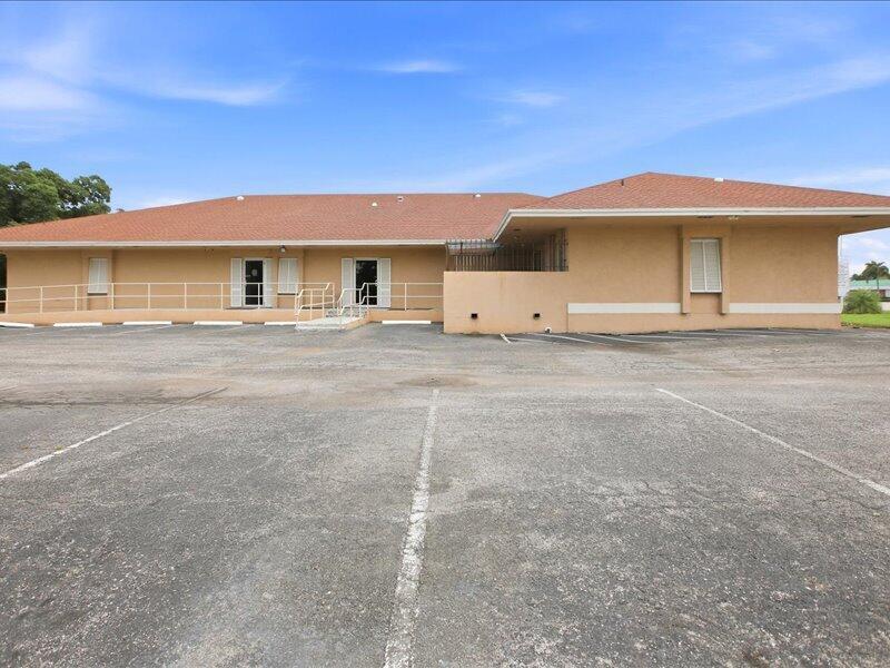 A single-story tan commercial building with a brown shingled roof and a large parking lot — 1100 S Main Street, Belle Glade FL 33430, BELLE GLADE, FL