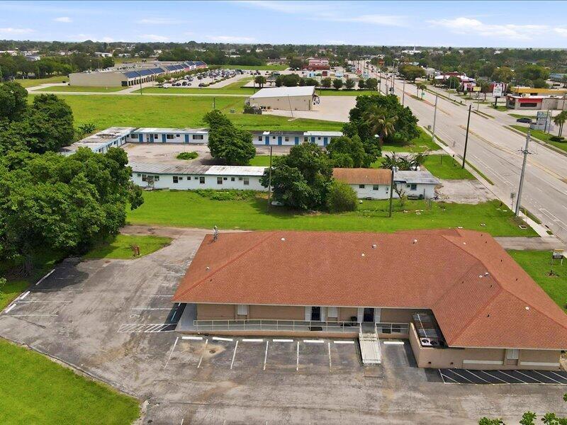 An aerial view shows a commercial building with a red roof and adjacent motel structures — 1100 S Main Street, Belle Glade FL 33430, BELLE GLADE, FL