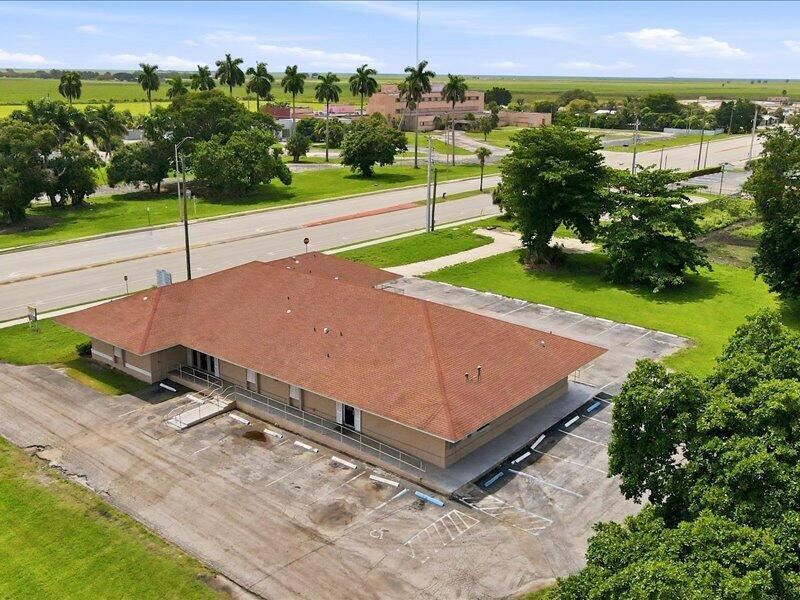 An aerial view shows a single-story commercial building with a brown roof and parking lot — 1100 S Main Street, Belle Glade FL 33430, BELLE GLADE, FL