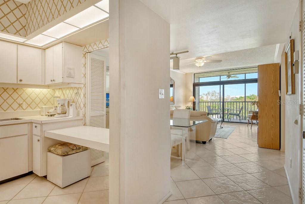 A dining area with a glass table and white chairs sits adjacent to a kitchen — 1945 GULF OF MEXICO DRIVE UNIT M2-402, LONGBOAT KEY, FL