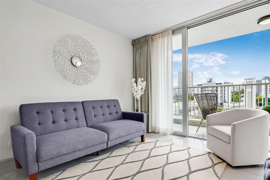 A living room features a purple sofa, a white armchair, and a balcony with city views — 1477 ASHFORD UNIT 608, SAN JUAN, PR